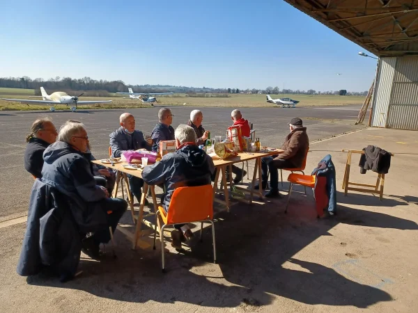 Pause dejeuner au club, groupe attable devant le hangar avec ULM en arriere-plan